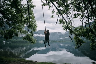 Caucasian woman swinging on rope swing at lake