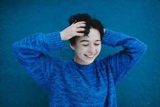 Smiling Caucasian woman tousling hair near blue wall