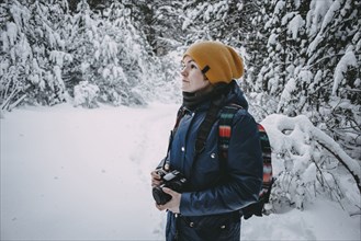 Caucasian woman holding camera in snowy forest