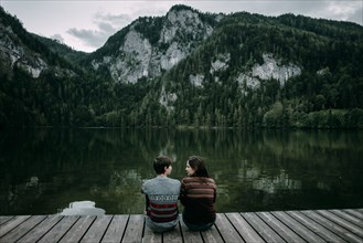 Caucasian couple sitting on dock near scenic view of mountain