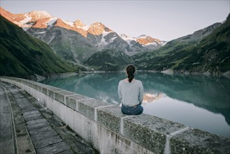 Caucasian woman sitting on wall at mountain lake