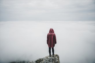 Distant Caucasian woman standing on rock watching fog on ocean