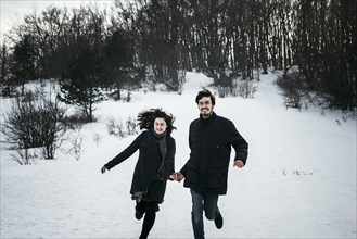 Caucasian couple running from forest in winter