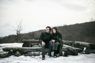 Caucasian couple sitting on logs in winter
