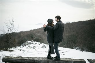 Caucasian couple dancing on log in winter