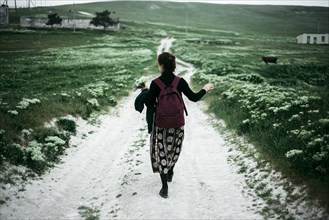Caucasian woman walking on dirt road carrying wildflowers