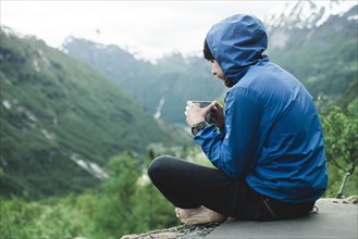 Caucasian man sitting in mountain landscape drinking coffee