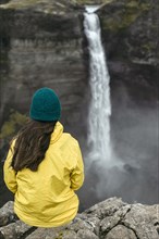 Caucasian woman sitting on cliff admiring waterfall