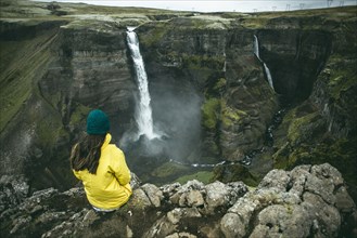 Caucasian woman sitting on cliff admiring waterfalls