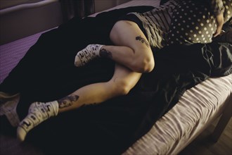 Caucasian woman laying on bed with tattoos on legs
