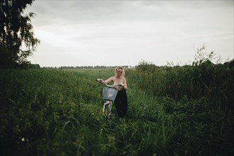 Caucasian woman pushing a bicycle in field