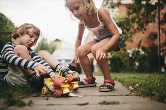 Caucasian girl helping boy with rollerskates