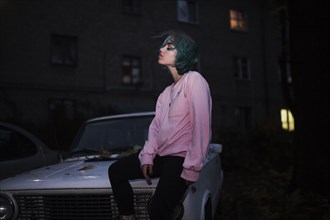 Caucasian woman sitting on hood of car at night
