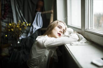 Portrait of pensive Caucasian woman leaning on window sill