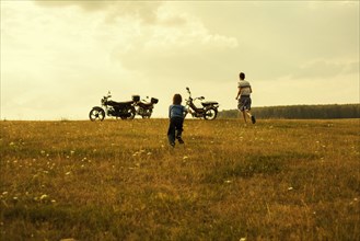 Boys running to motorcycles in rural landscape