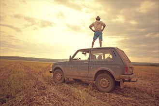 Mari man standing on car roof in rural field