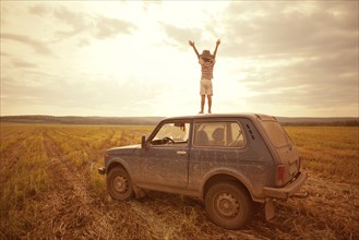 Mari boy standing on car roof in rural field