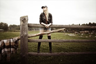 Caucasian woman standing on wooden fence at ranch