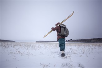 Mixed race man carrying skis in snowy field