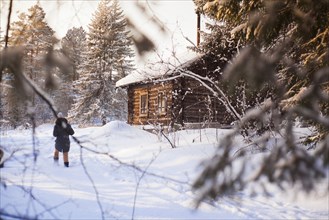 Caucasian woman walking near log cabin in snowy forest