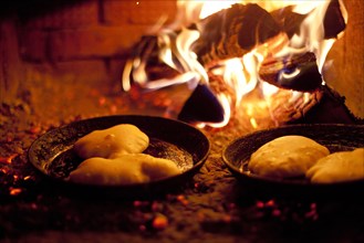 Close up of pastries cooking in skillets near wood fire