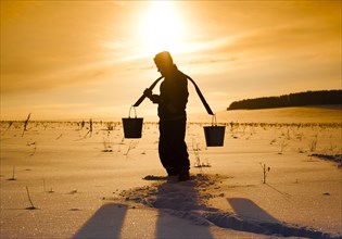 Silhouette of Mari man carrying buckets on traditional yoke in snowy field