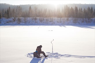 Mari man ice fishing in snowy field