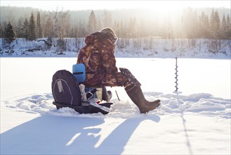 Mari man ice fishing in snowy field