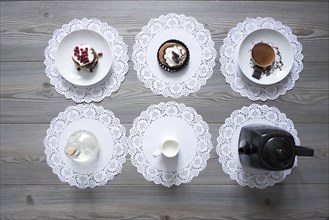 Teapot and plates of dessert on lace doilies