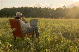 Mari man sitting on chair in field using laptop