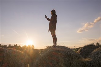 Caucasian woman standing on hay holding cell phone