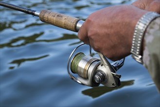 Hands of Mari man holding fishing rod in river