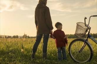Mother and son holding hands in field near bicycle
