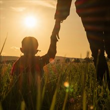 Woman and son holding hands in field at sunset