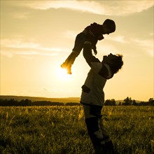 Mari man lifting son in field at sunset