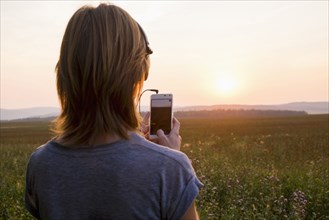 Caucasian woman photographing sunset with cell phone