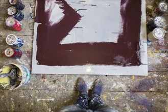 Legs of Mari man standing near paint cans and canvas on floor