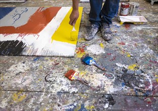 Legs of Mari man painting canvas on floor