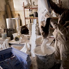 Caucasian artist pouring plaster mix into bucket