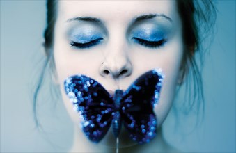 Caucasian teenage girl covering mouth with blue butterfly