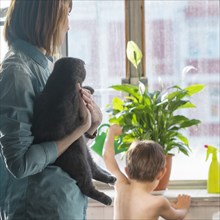 Caucasian mother holding cat watching son watering plant