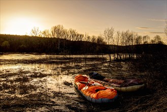 Inflatable rafts on shore of river at sunset
