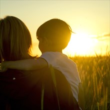 Mother carrying son in field of wheat at sunset