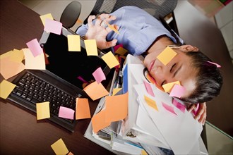 Hispanic businesswoman covered in sticky notes sleeping at desk