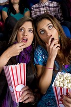 Hispanic friends enjoying popcorn in movie theater