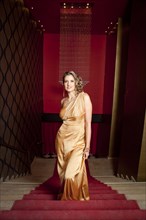 Glamorous Hispanic woman in evening gown standing on stairs
