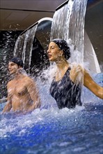 Hispanic couple enjoying waterfall in swimming pool
