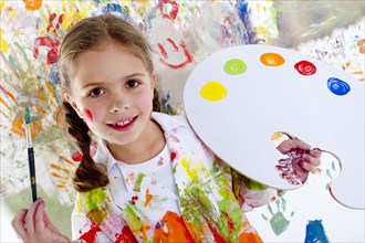 Hispanic girl covered in paint holding paintbrush