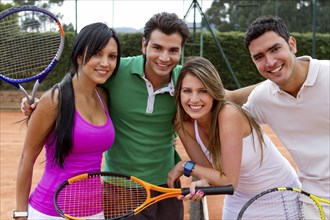 Hispanic couples smiling near tennis court net