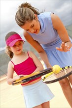 Hispanic woman teaching girl to play tennis